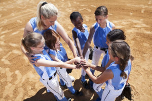 Softball players with coach in huddle doing team cheer