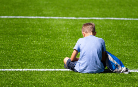 child sitting on a football field with a backpack