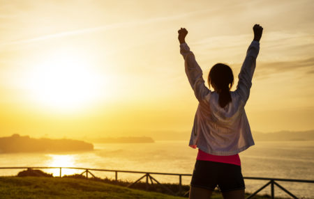 woman cheering with her arms up at a sunset