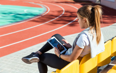 photo of a woman sitting by a running track using her Ipad